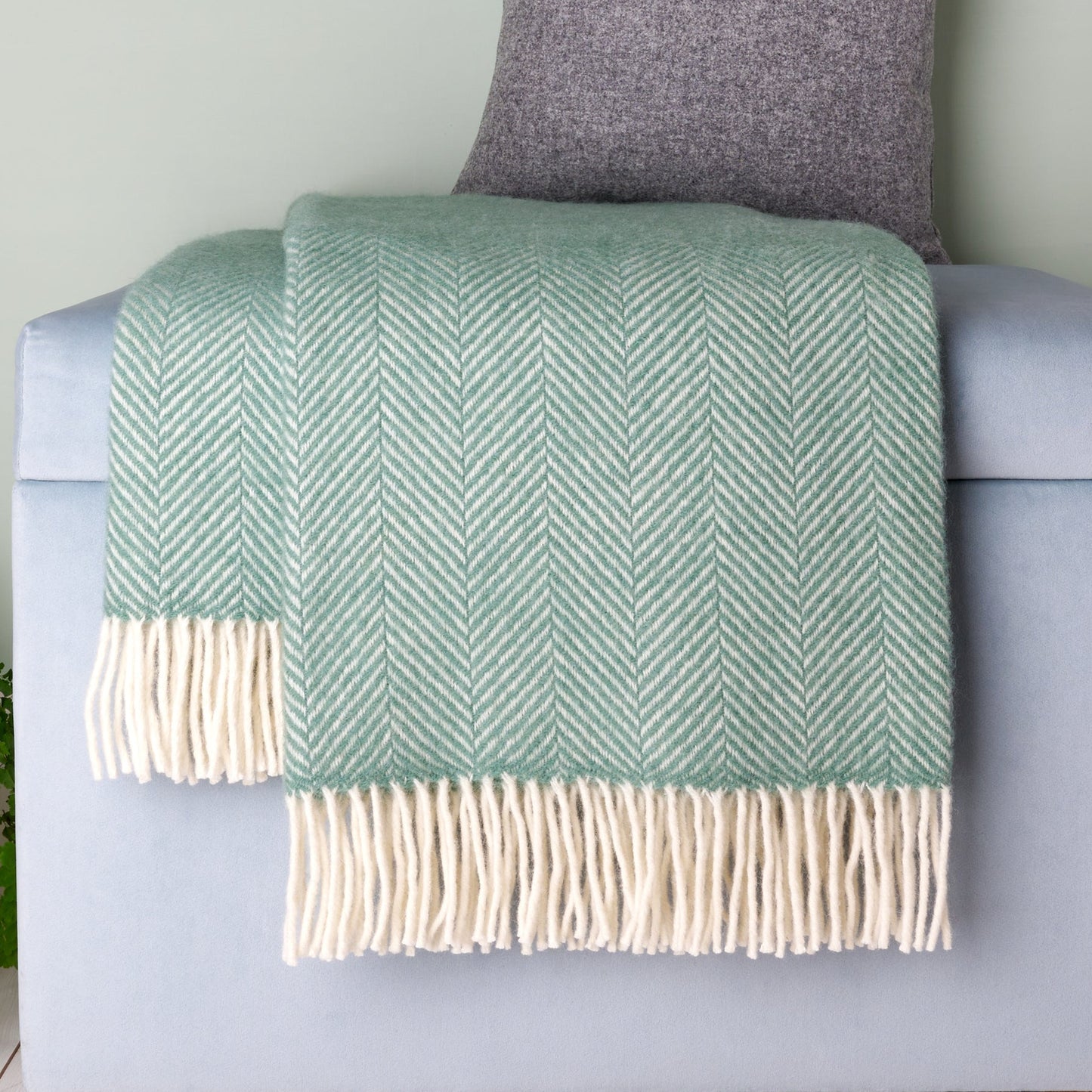 Green herringbone blanket with white fringes draped over a gray armchair.