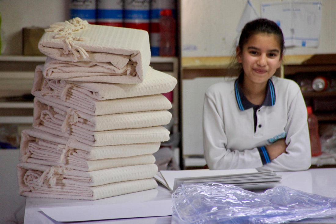Stacks of folded white towels on a packing desk with a smiling mill employee