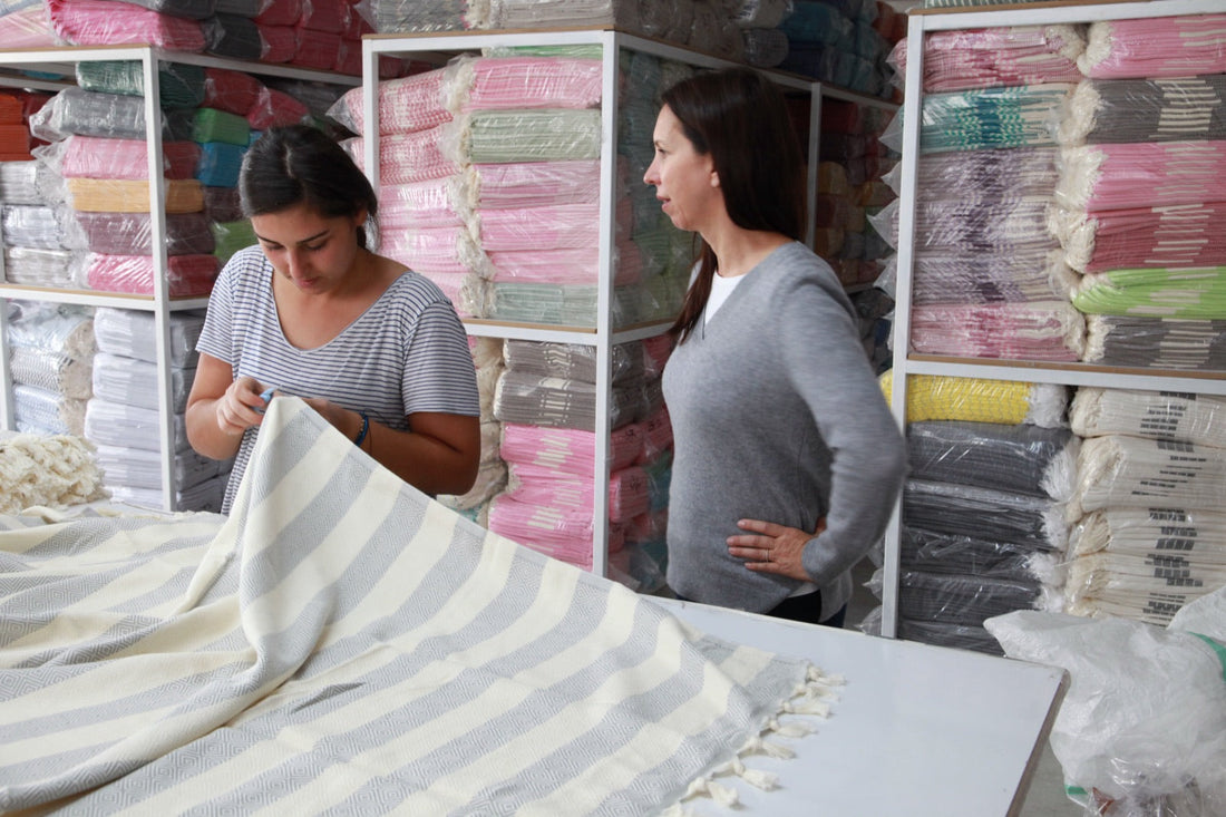 A woman reviewing striped towels at a table with a laptop in a mill showroom