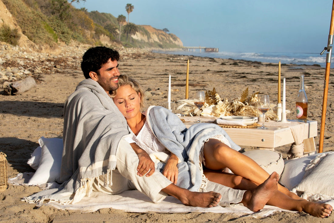 A couple wrapped in a grey blanket at a beach picnic