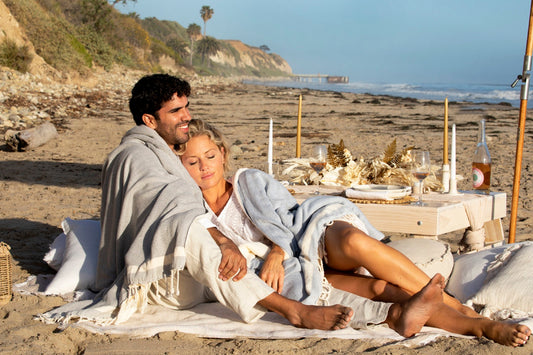 A couple wrapped in a grey blanket at a beach picnic