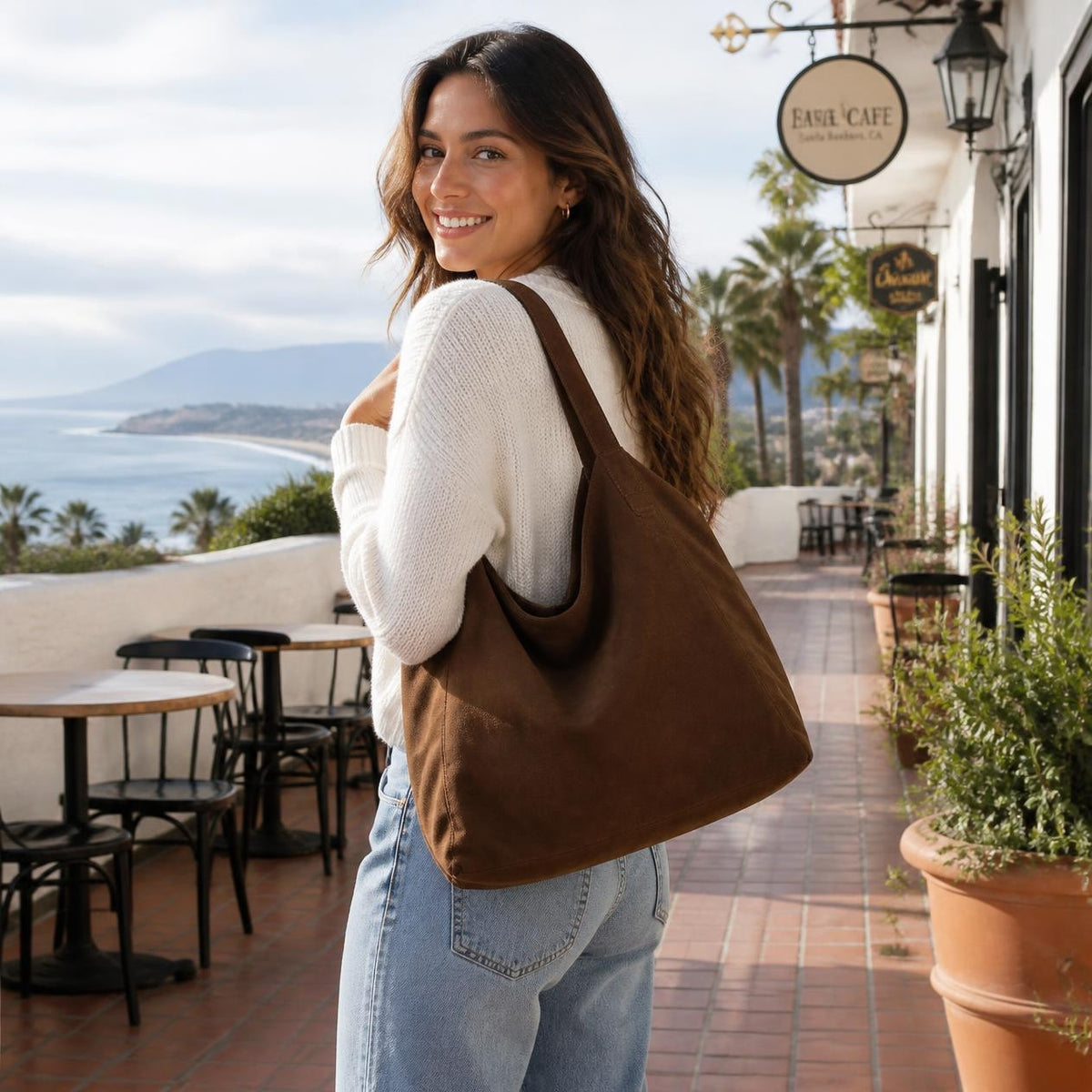 Woman carrying the Coco Marbella suede tote on an ocean-view terrace