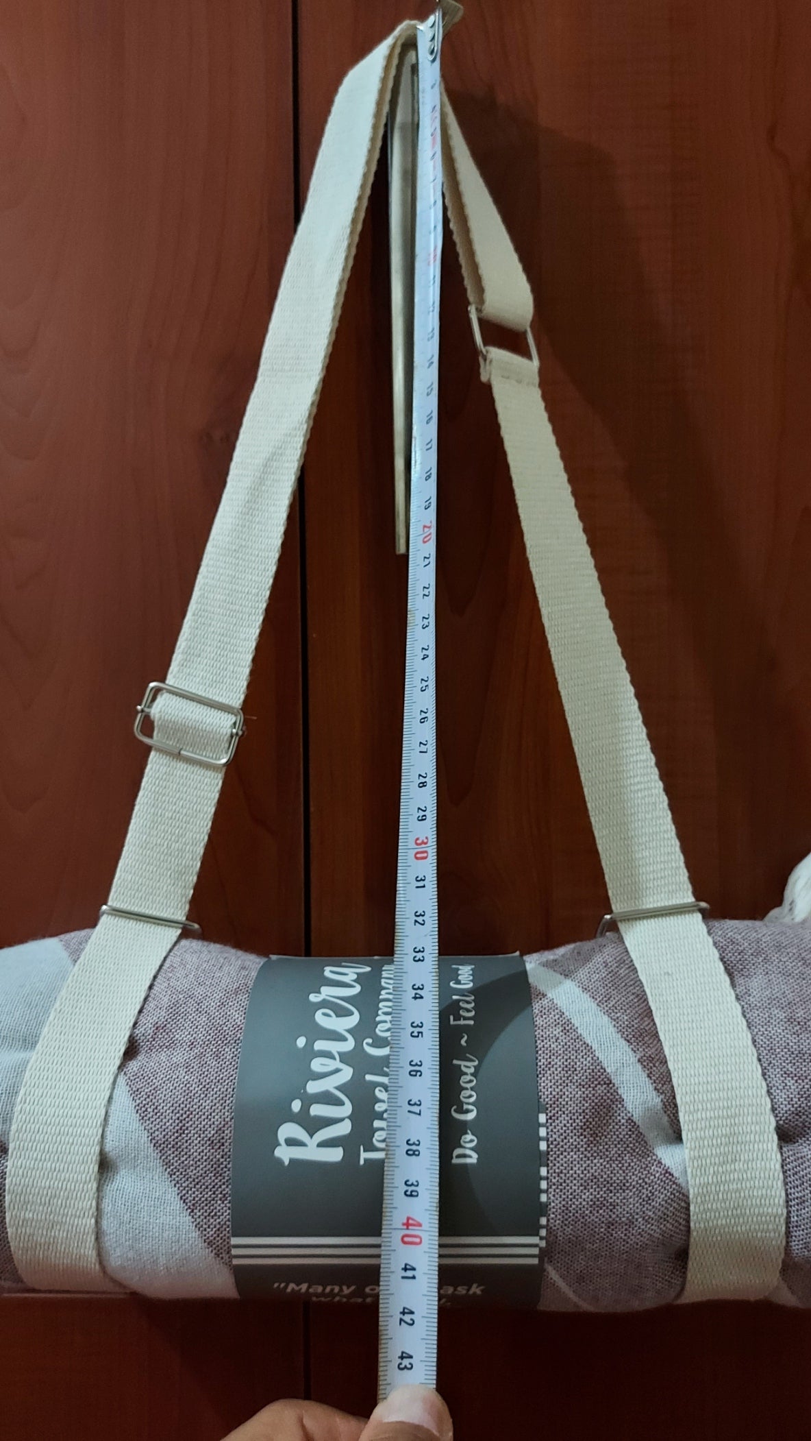Measuring tape being used to measure a strap on a bag against a wooden surface.