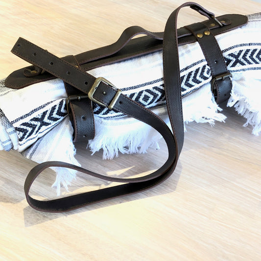 Black leather strap with a buckle on a white towel with blue patterns, placed on a wooden surface.