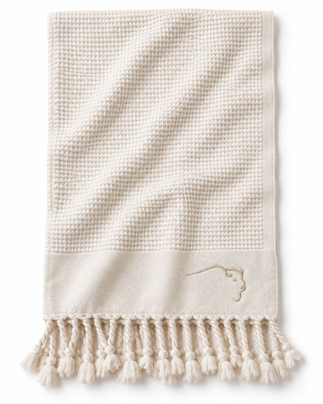 An off-white waffle-weave towel with a solid border, decorative fringe tassels, and a small embroidered logo on the lower right, shown against a plain white background.