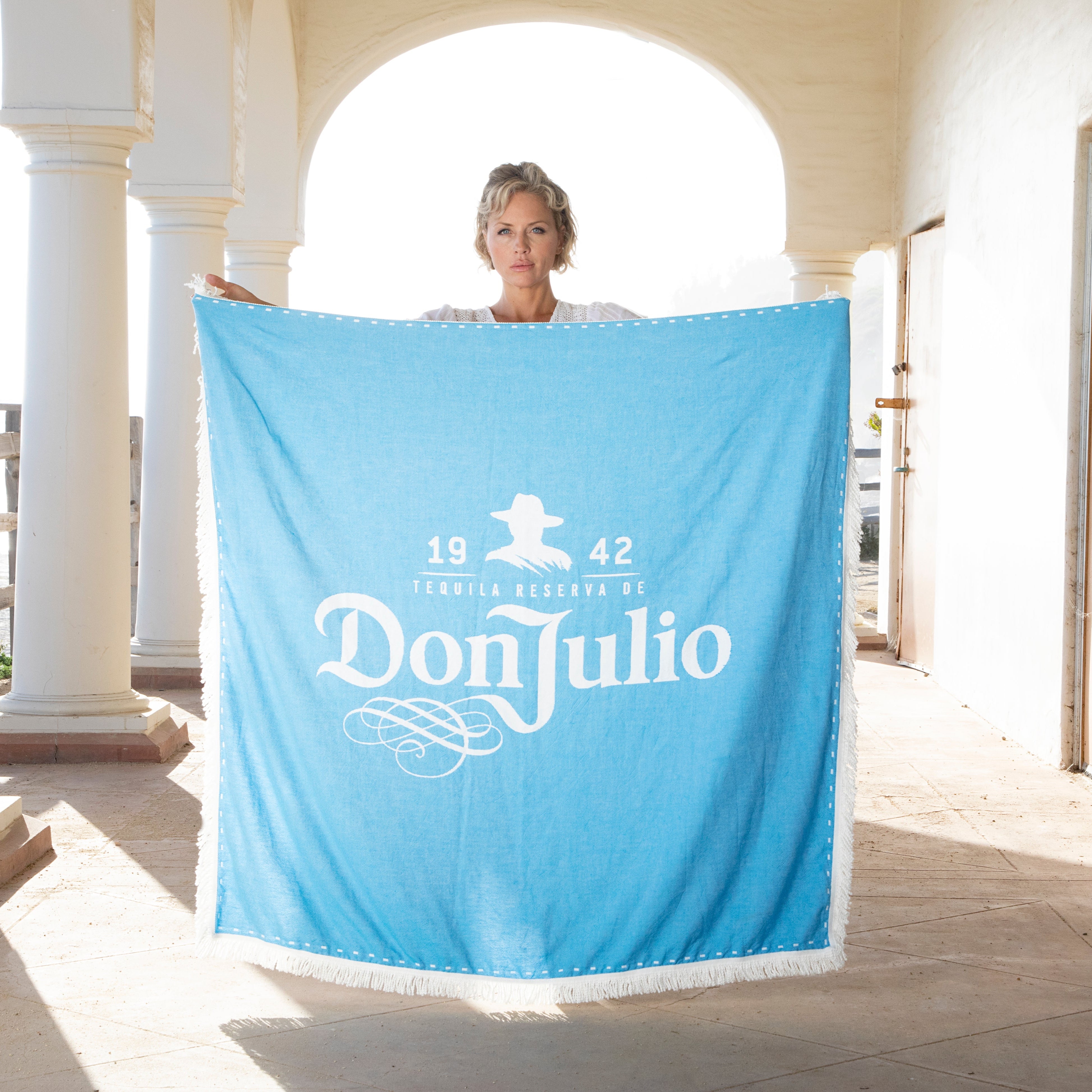 Person holding a blue towel with 'Don Julio' branding on a white architectural background