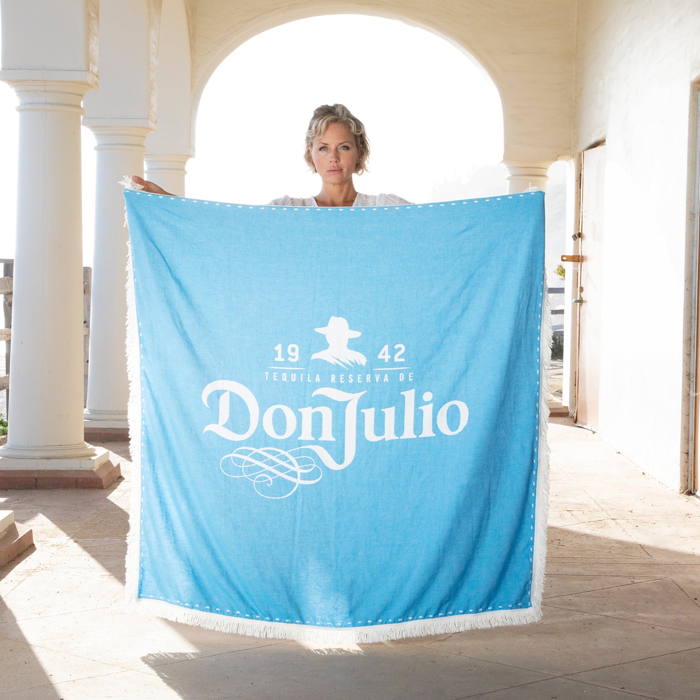 Person holding a blue towel with 'Don Julio' branding on a white architectural background