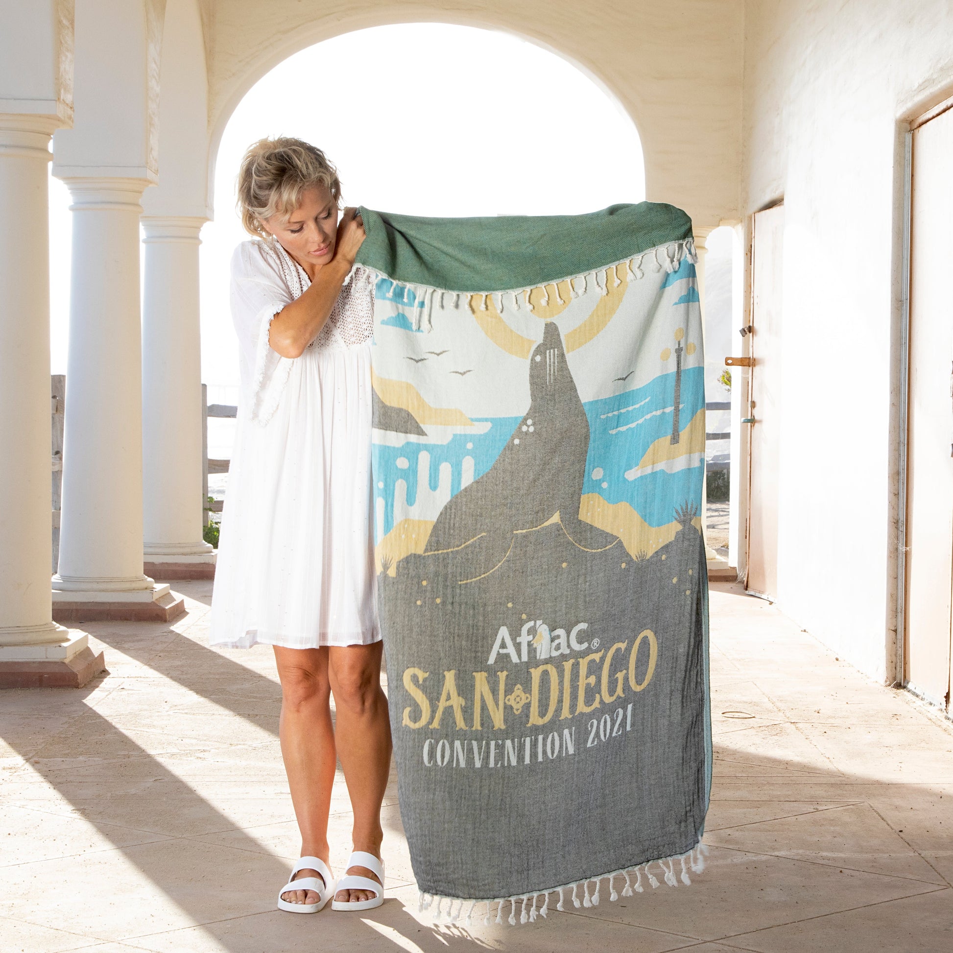 Woman holding an Aflac branded towel with a design and text in an outdoor setting