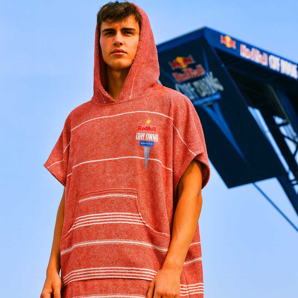 Person wearing a red hooded towel poncho with a visible brand logo against a blue sky.