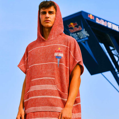 Person wearing a red hooded towel poncho with a visible brand logo against a blue sky.