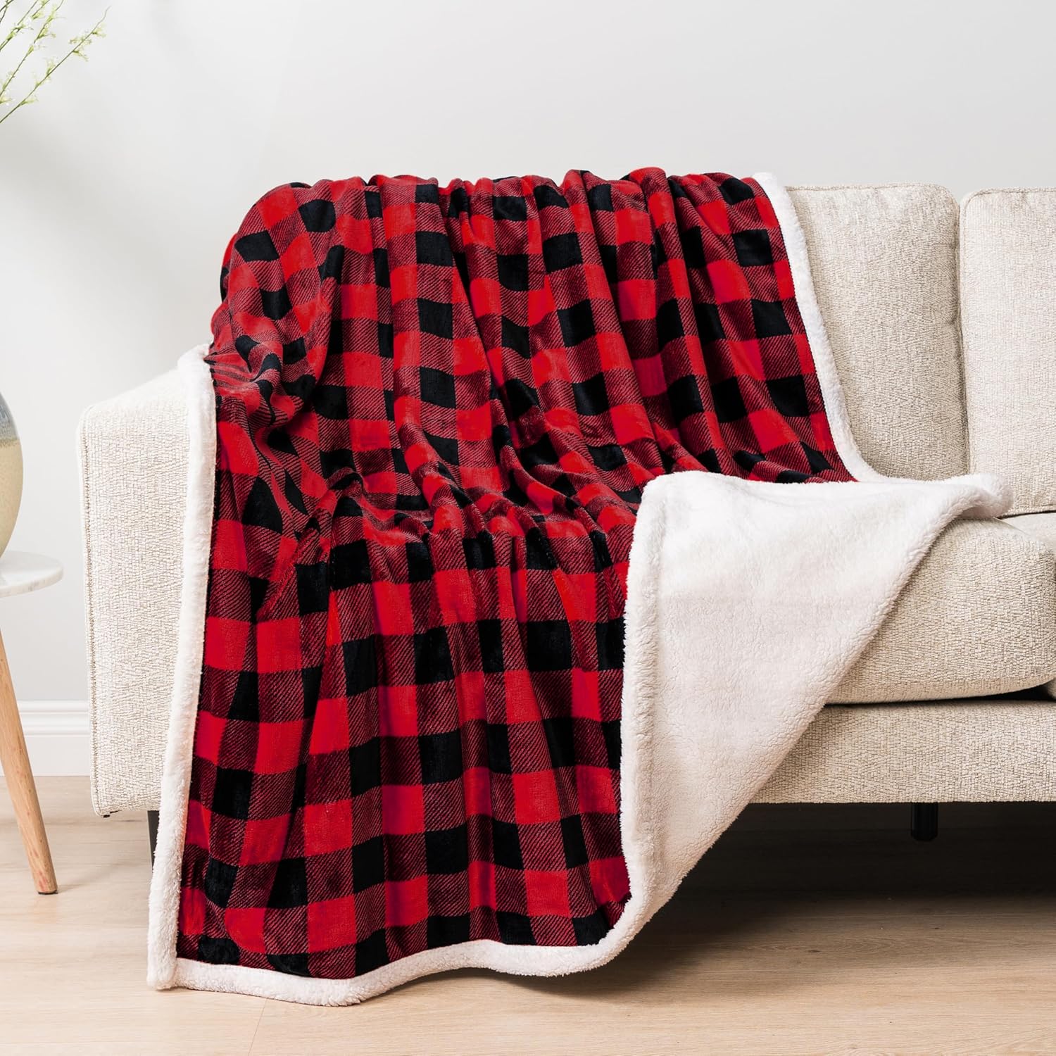 Red and black plaid blanket draped over a beige sofa in a living room setting.