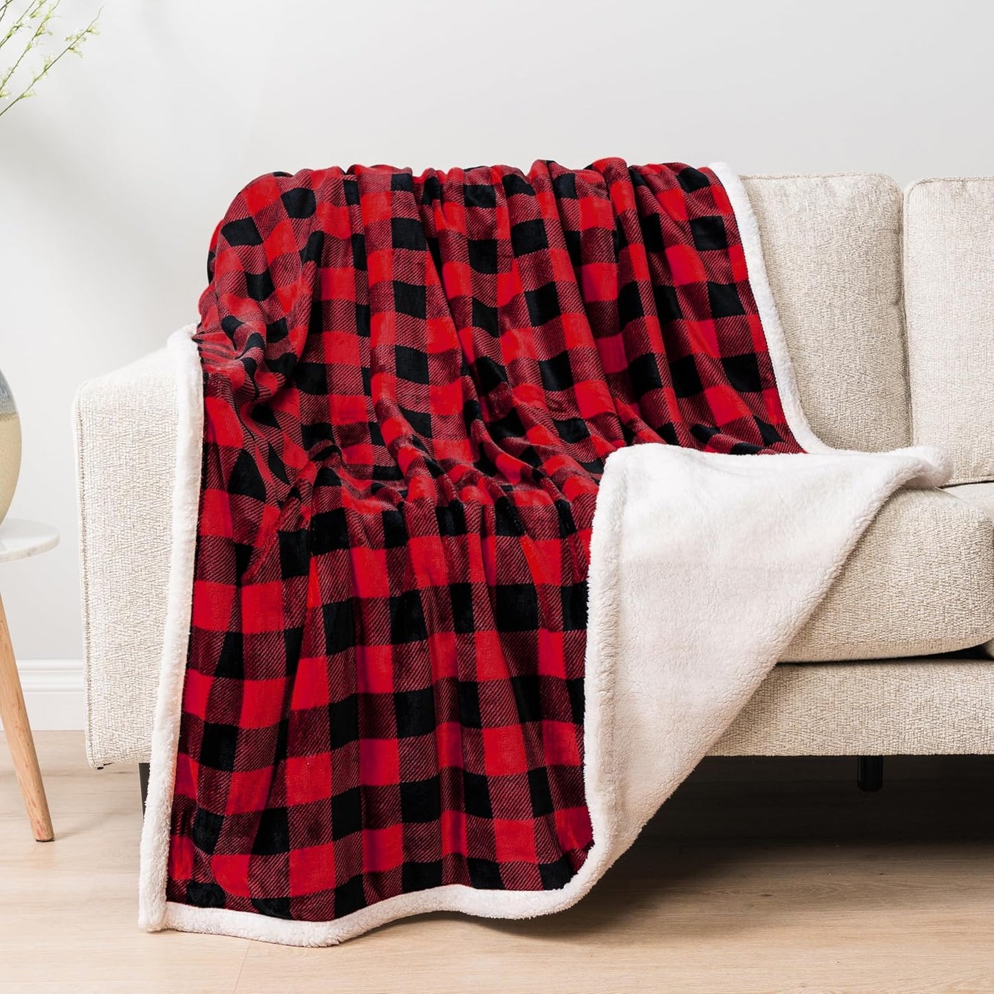 Red and black plaid blanket draped over a beige sofa in a living room setting.