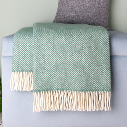 Green herringbone blanket with white fringes draped over a gray armchair.
