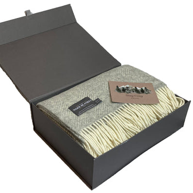 Woven blanket in a gray gift box with a brand label on a white background
