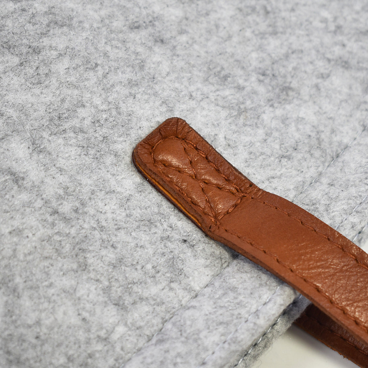 Close-up of the stitched cognac handle on light gray wool